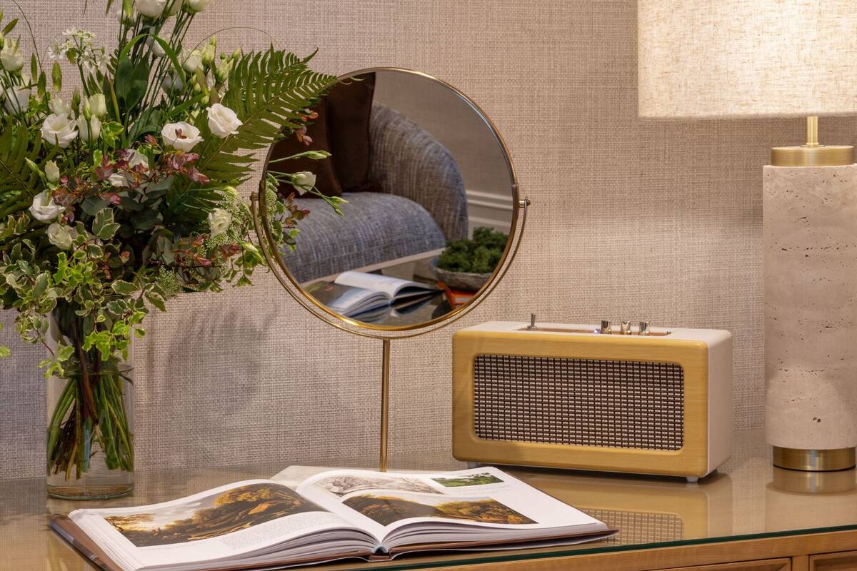 A room with a mirror, a vintage radio, a book, and a floral arrangement.