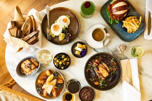 Une variété de plats, notamment des œufs, des frites et un hamburger, disposés sur une table avec du pain et des boissons.