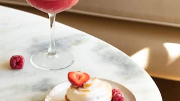 A dessert with raspberries and a glass of a pink drink on a marble table.