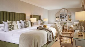 Une chambre d’hôtel avec un grand lit, deux tables de chevet, un miroir, un bureau avec une chaise et une petite table sur laquelle est posé un vase.