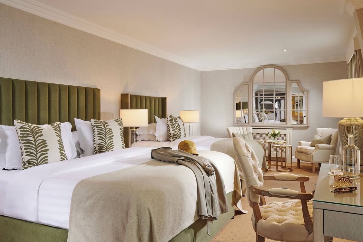 A hotel room with a large bed, two bedside tables, a mirror, a desk with a chair, and a small table with a vase.