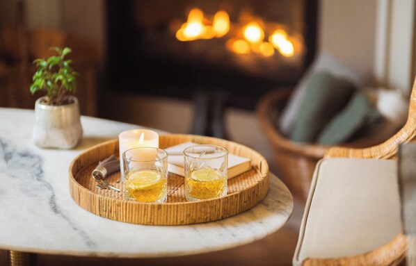 A cozy indoor setting with a fireplace, a tray with glasses and a candle, and a small potted plant.