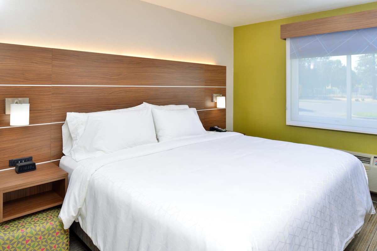 A hotel room with a large bed, a wooden headboard, bedside lamps, and a window with a view.