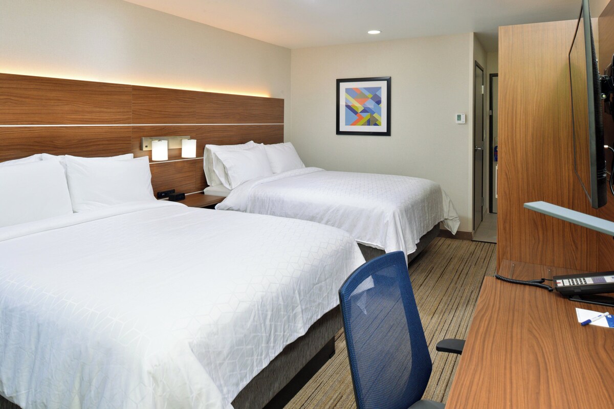 A hotel room with two beds, a desk with a telephone, and a wall-mounted TV.