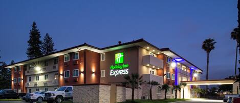 Een Holiday Inn Express gebouw met een bakstenen gevel, meerdere ramen en een parkeerplaats met diverse auto's.