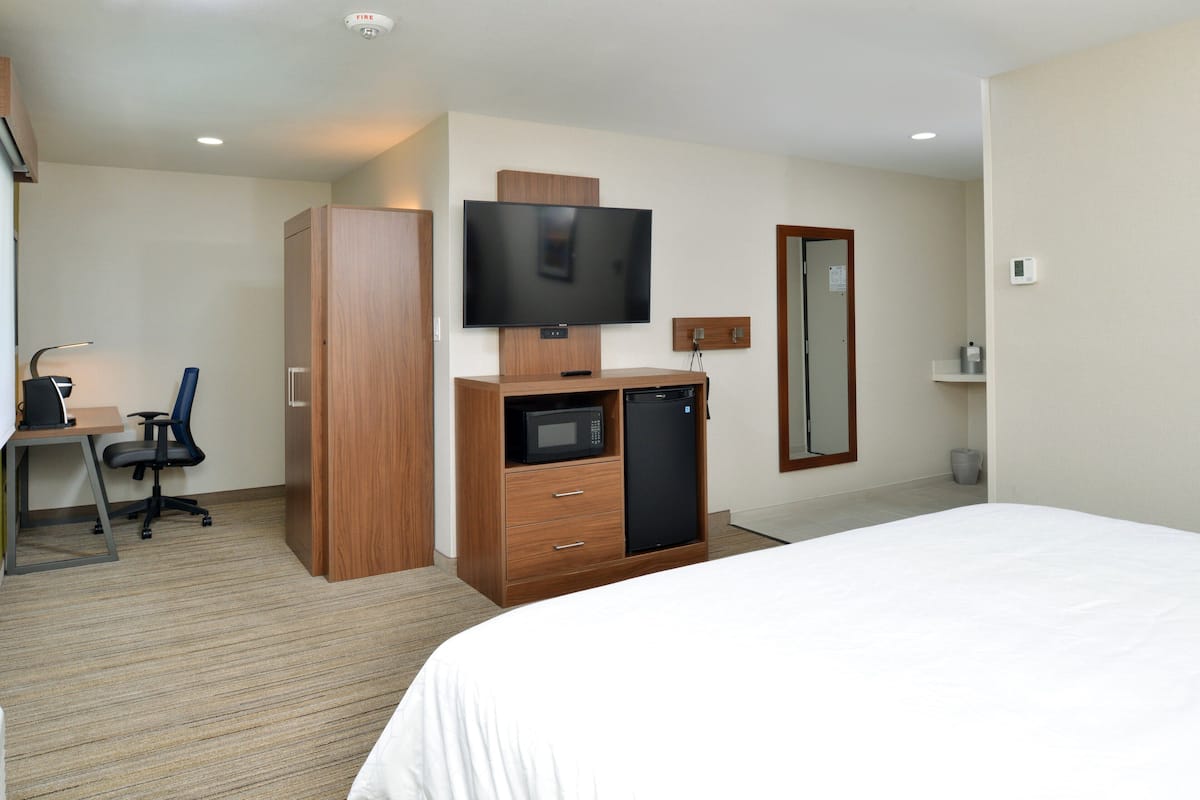 A hotel room with a bed, a desk with a chair, a television, a microwave, a refrigerator, and a wardrobe.