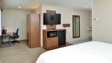 A hotel room with a bed, a desk with a chair, a television, a microwave, a refrigerator, and a wardrobe.
