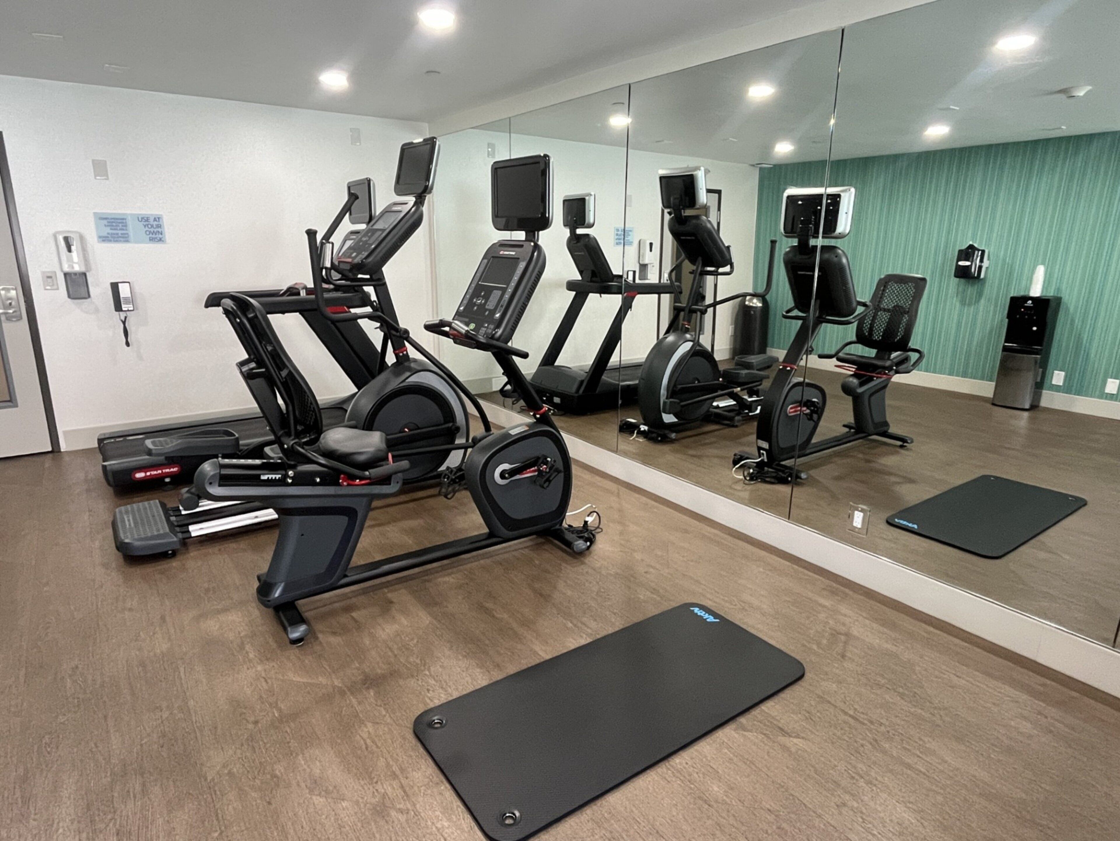 Uma academia com máquinas de cardio, espelhos e colchonetes pretos.