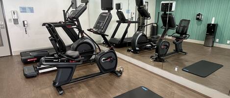 Uma academia com máquinas de cardio, espelhos e colchonetes pretos.