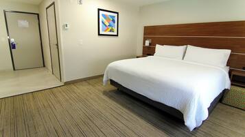 A hotel room with a large bed, a wooden headboard, a framed picture on the wall, and a door to the left.