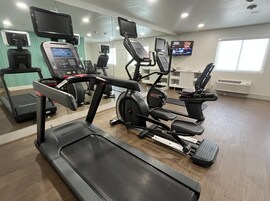 Un gimnasio con cintas de correr, elípticas y una bicicleta estática.