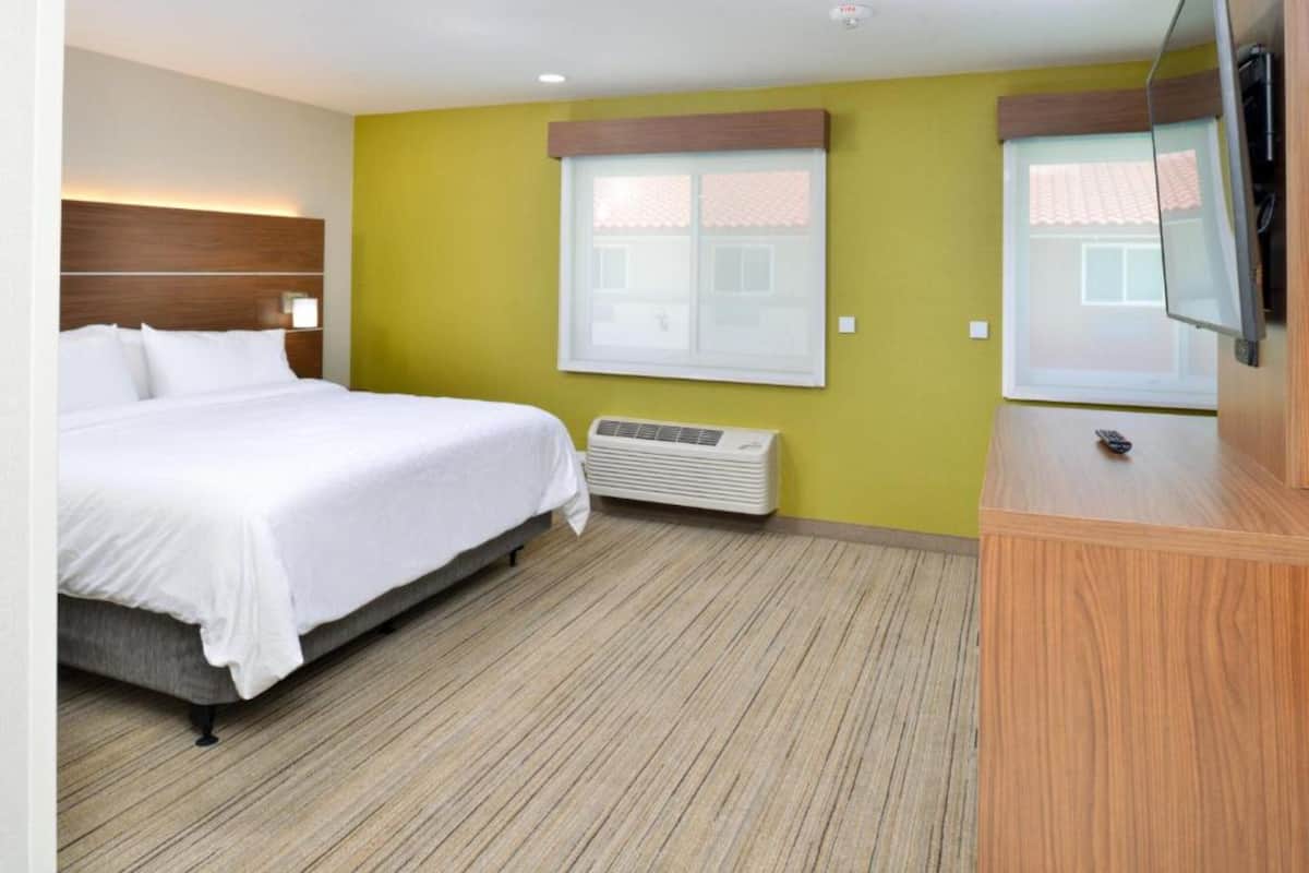 A hotel room with a bed, a TV, a window, and a wall-mounted heater.