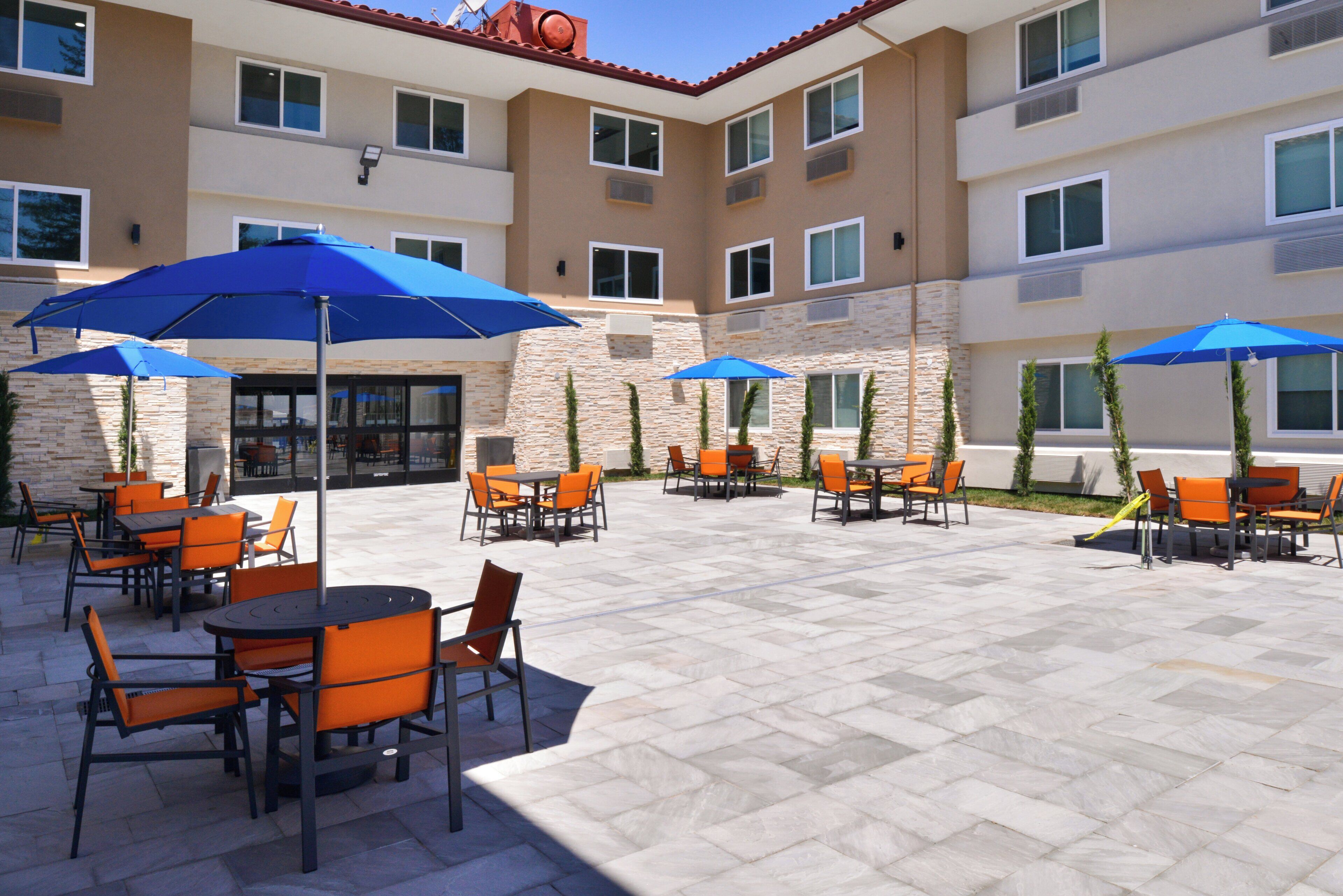An outdoor patio area with multiple tables and chairs, some shaded by umbrellas.