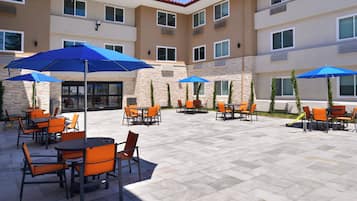 An outdoor patio area with multiple tables and chairs, some shaded by umbrellas.