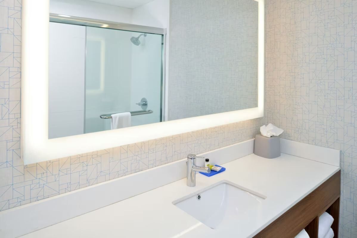 Een badkamer met een grote spiegel, een wastafel, een douchecabine van glas en een handdoekhouder.