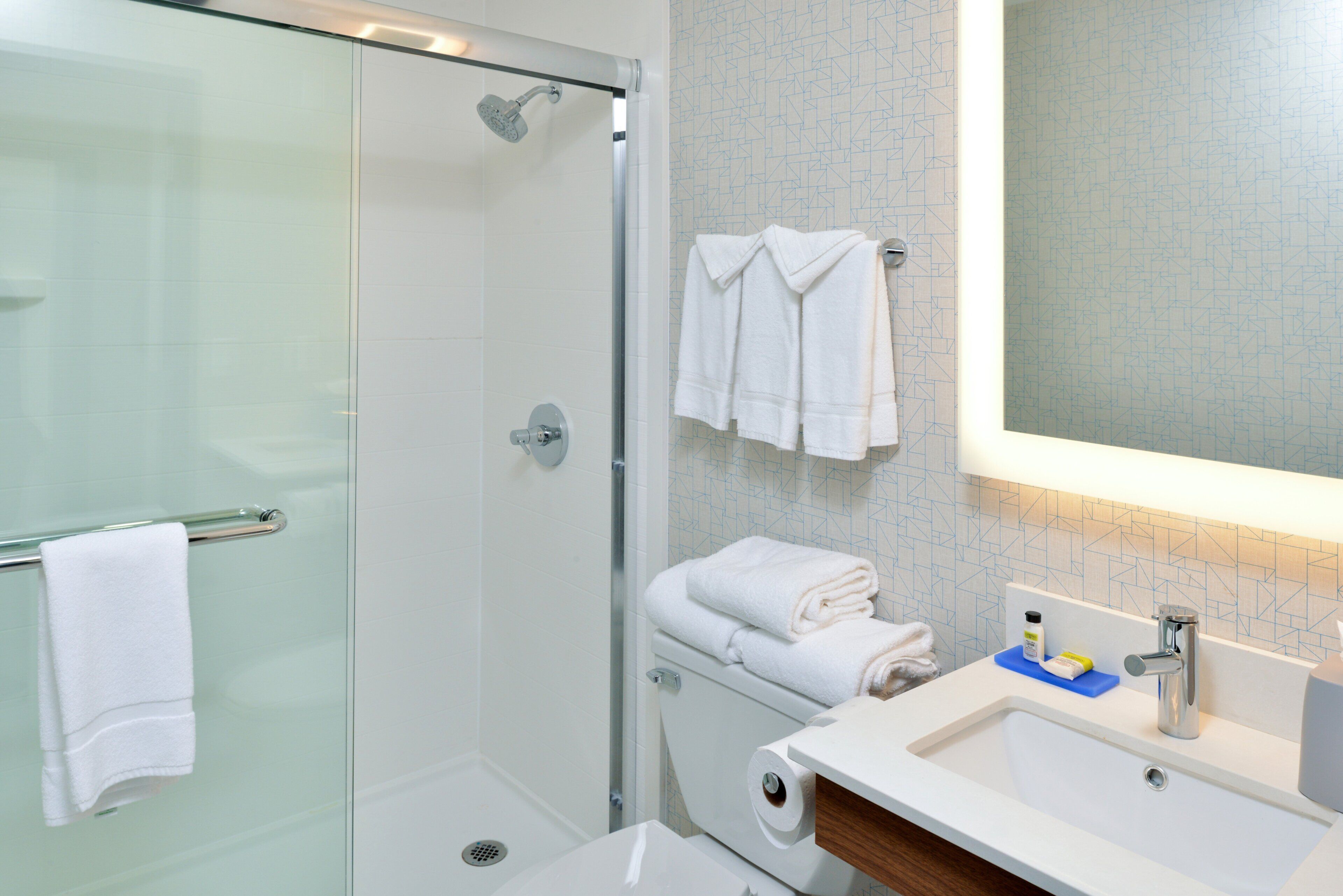 A modern bathroom with a glass shower enclosure, a white sink with a mirror, and a towel rack with folded towels.