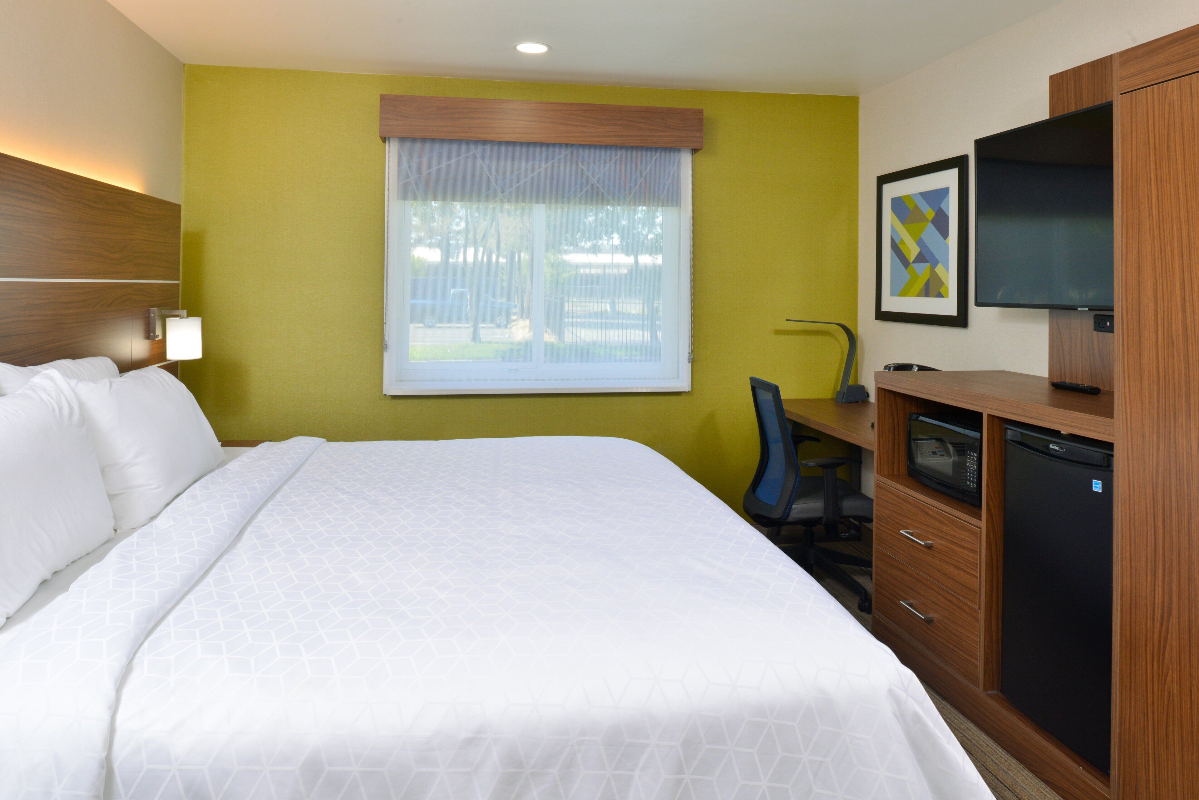 A hotel room with a bed, a desk, a television, and a window with a view of the outside.