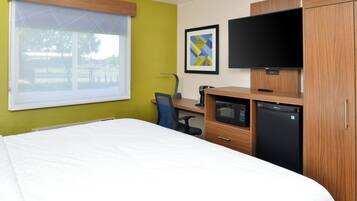 A hotel room with a bed, a desk with a computer, a television, and a refrigerator.
