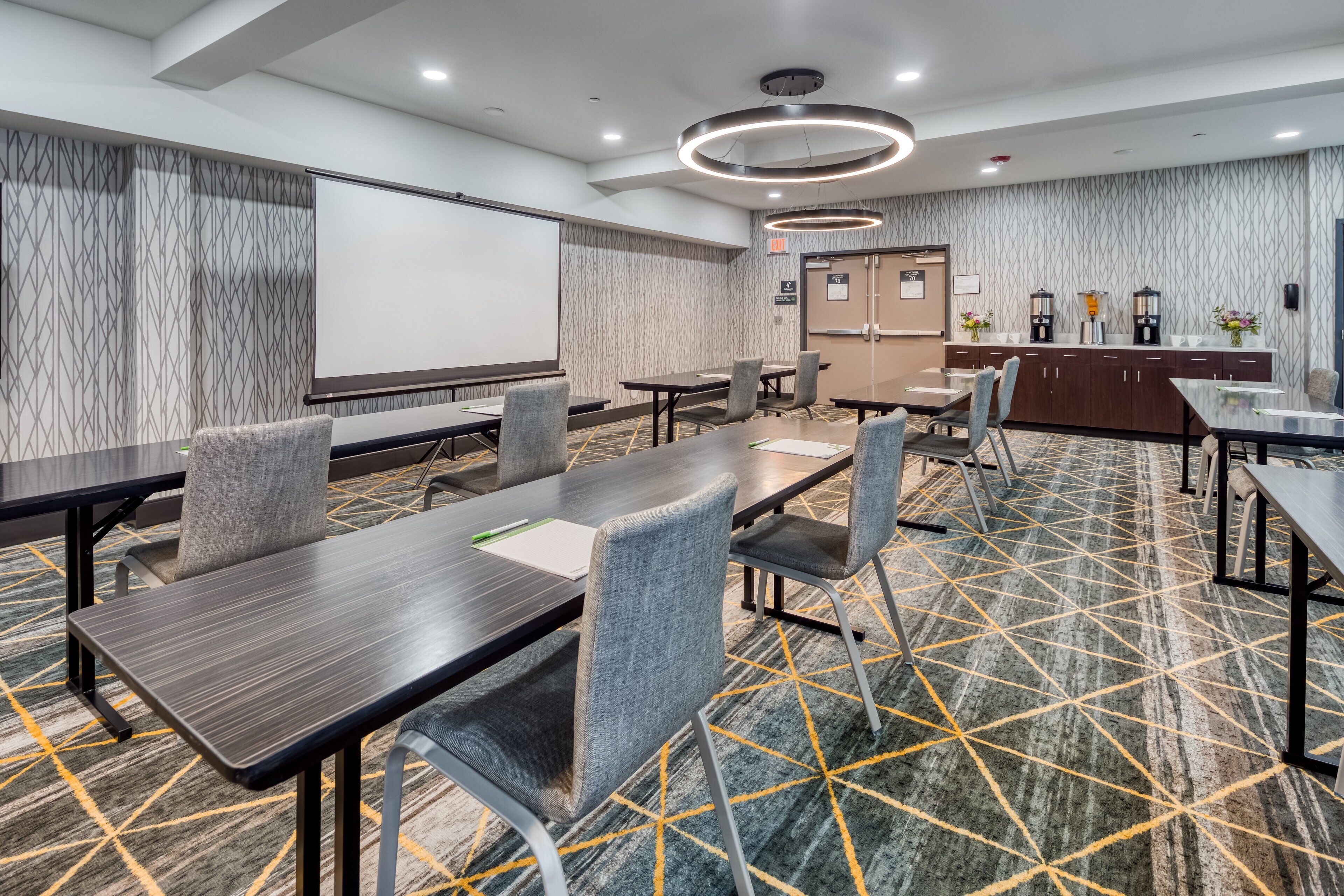 A conference room with a large table, chairs, a projector screen, and a coffee station.