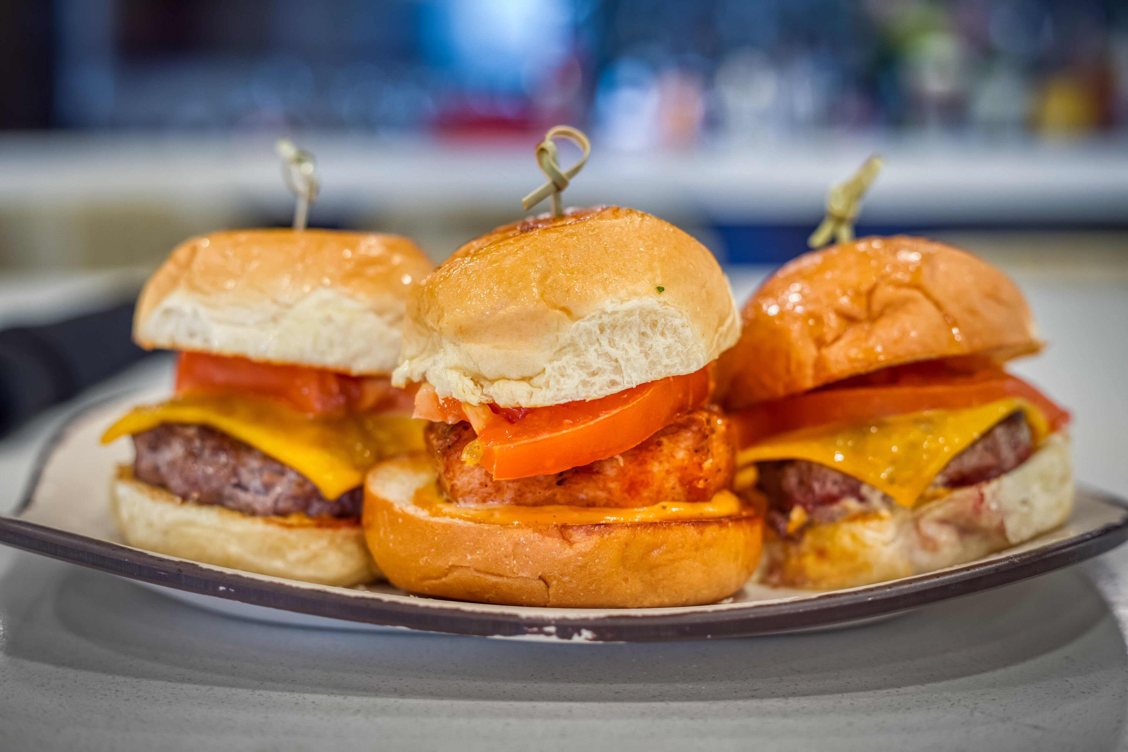Un plato con tres hamburguesas, cada una con pan, queso, tomate y una carne.