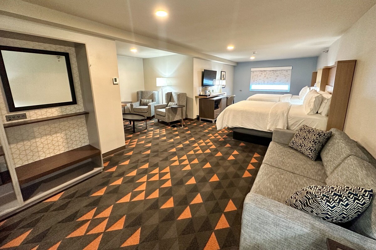 A hotel room with a bed, two armchairs, a desk, a television, and a patterned carpet.
