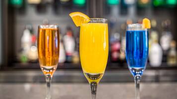 Trois verres de boissons sur le comptoir d’un bar, avec un arrière-plan flou composé de bouteilles.