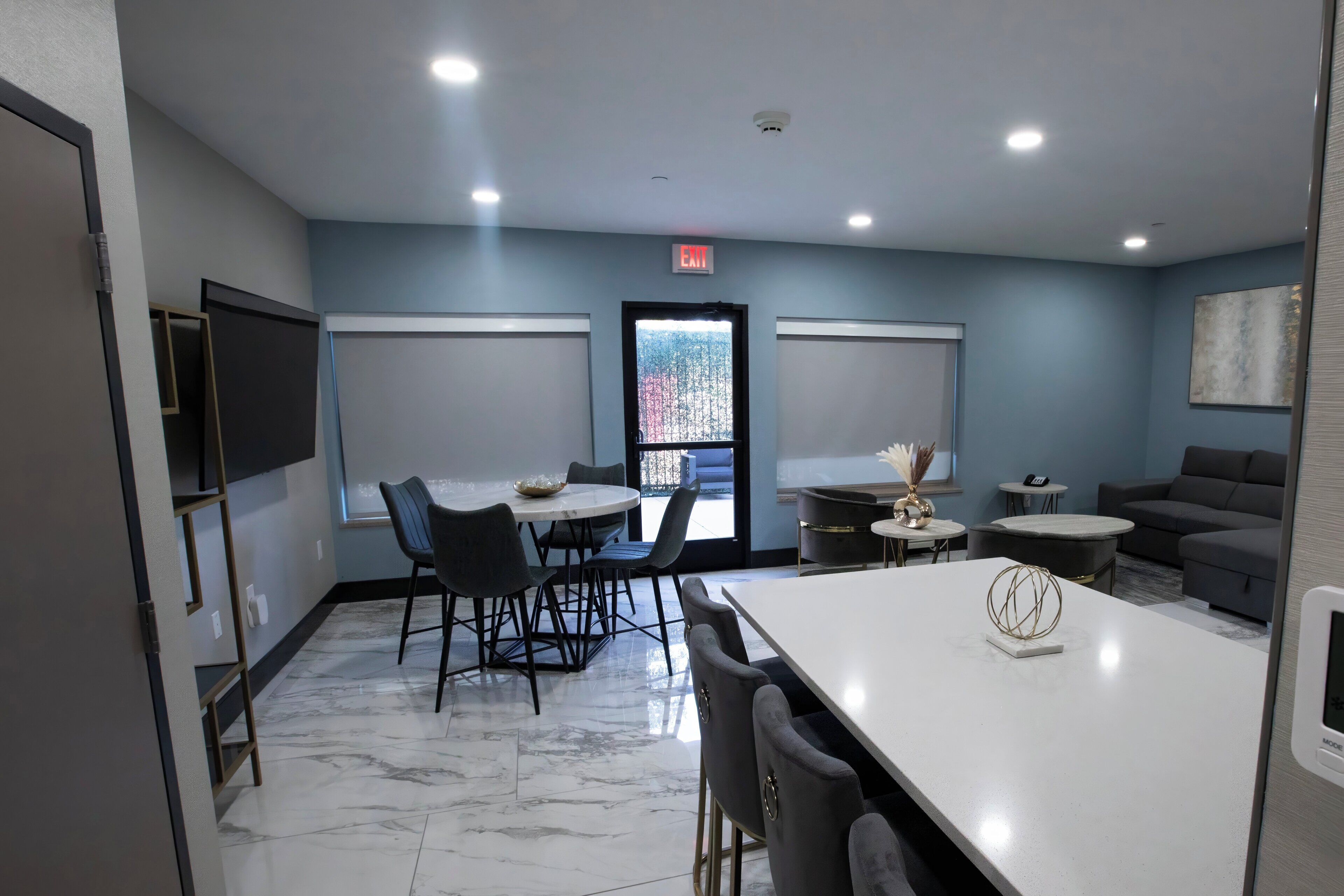 A modern hotel room with a marble floor, a dining area with a white table and chairs, a sofa, and a small decorative table with a vase.