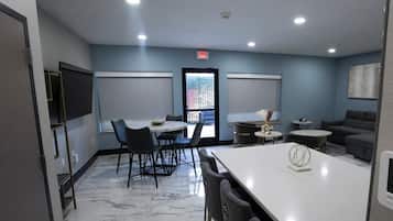 Une chambre d’hôtel moderne avec un sol en marbre, un coin repas comprenant une table et des chaises blanches, un canapé et une petite table d’appoint décorative surmontée d’un vase.
