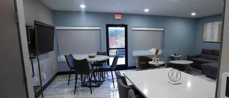 A modern hotel room with a marble floor, a dining area with a white table and chairs, a sofa, and a small decorative table with a vase.