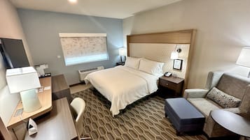 Una habitación de hotel con cama, mesita de noche, escritorio, silla y un pequeño sofá.