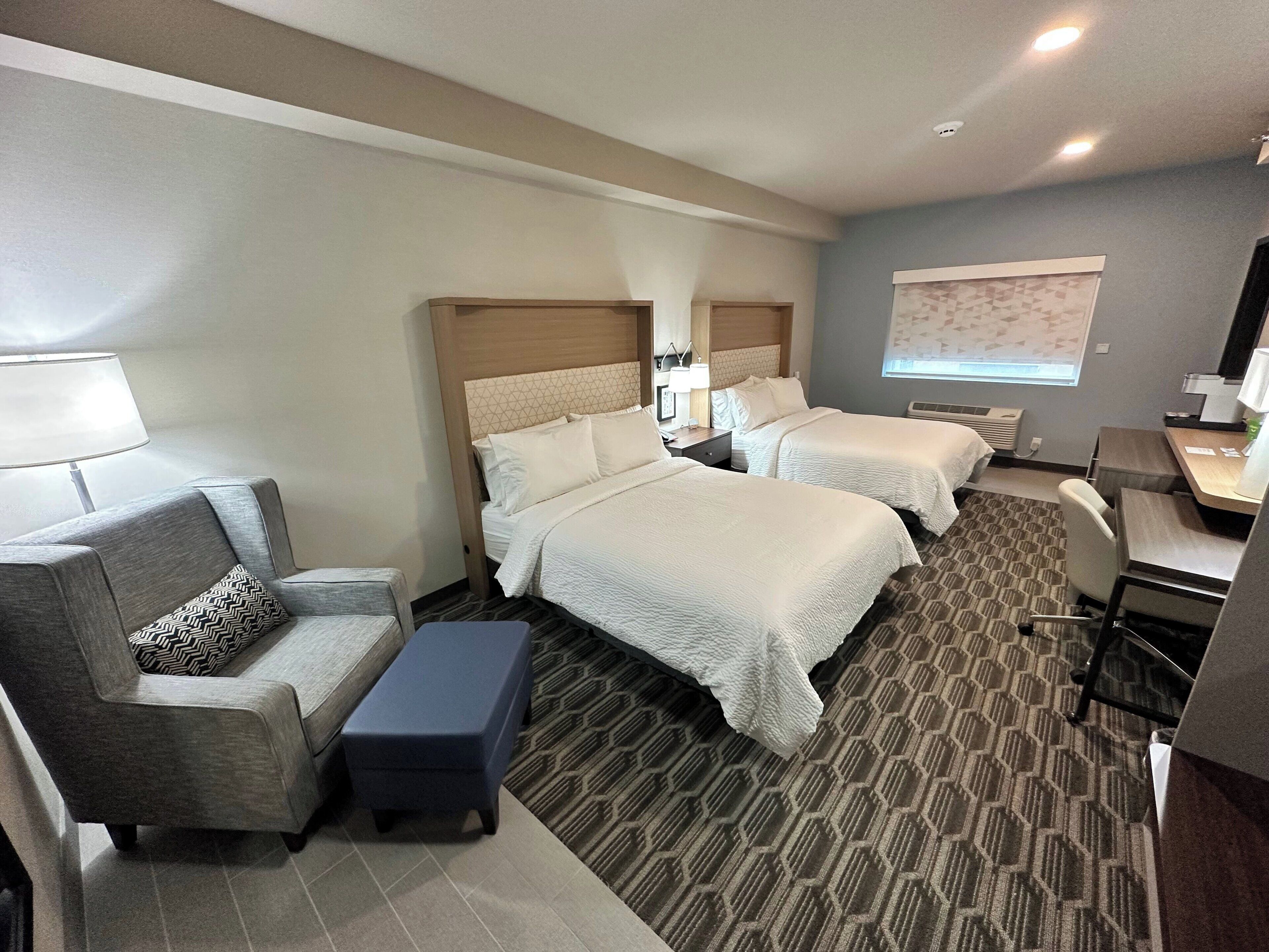 A hotel room with two beds, a desk, a chair, a sofa, and a patterned carpet.