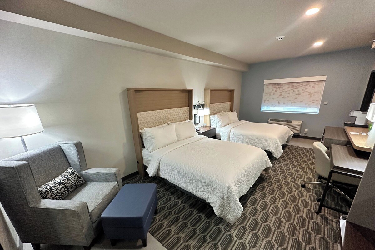 A hotel room with two beds, a desk, a chair, a sofa, and a small table.