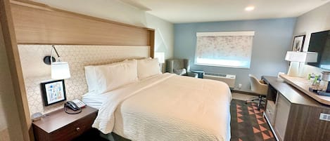 Una habitación de hotel con cama, mesita de noche, lámpara y escritorio con silla.