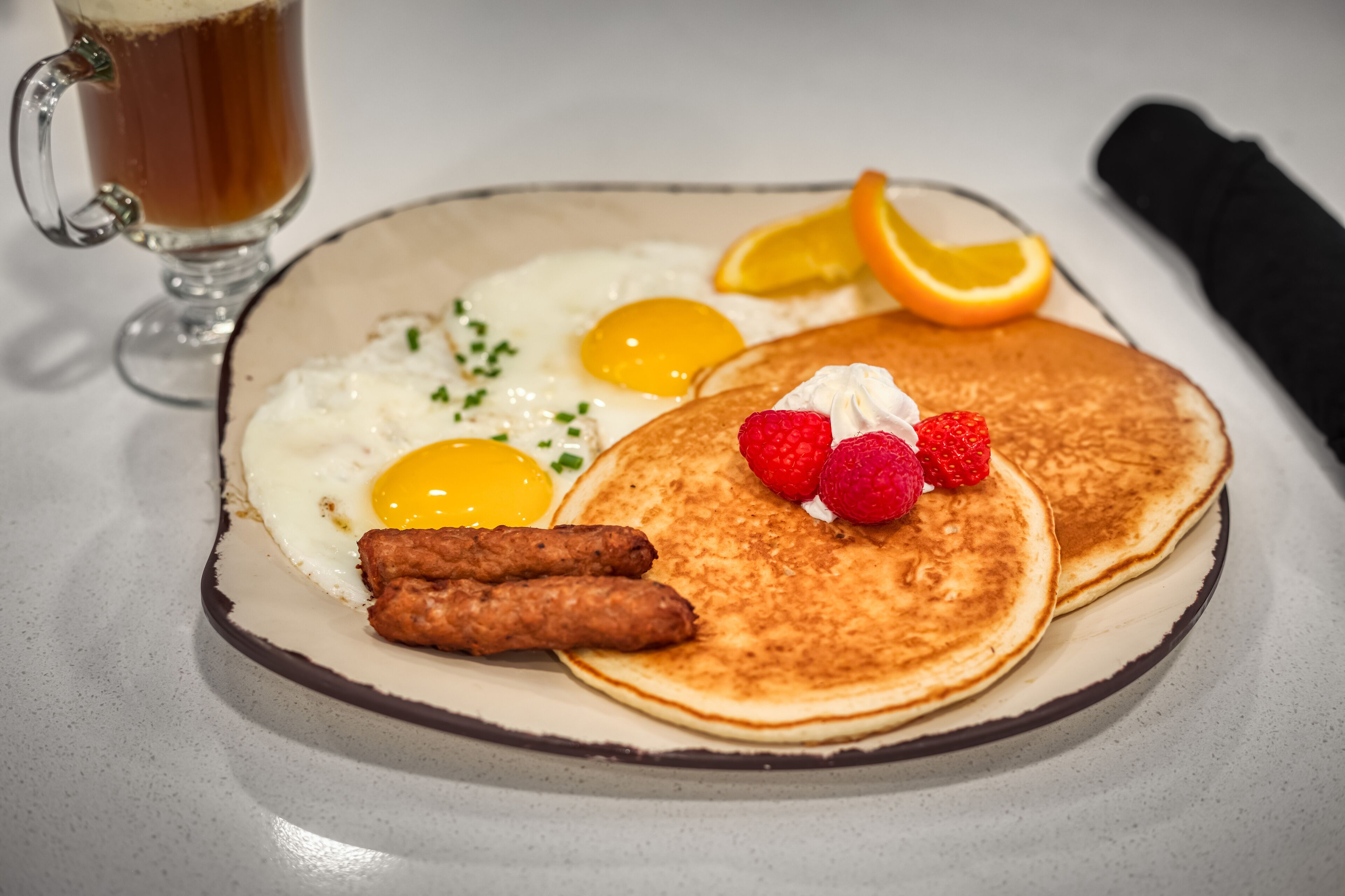 A breakfast plate with pancakes, eggs, sausage, and fruit.