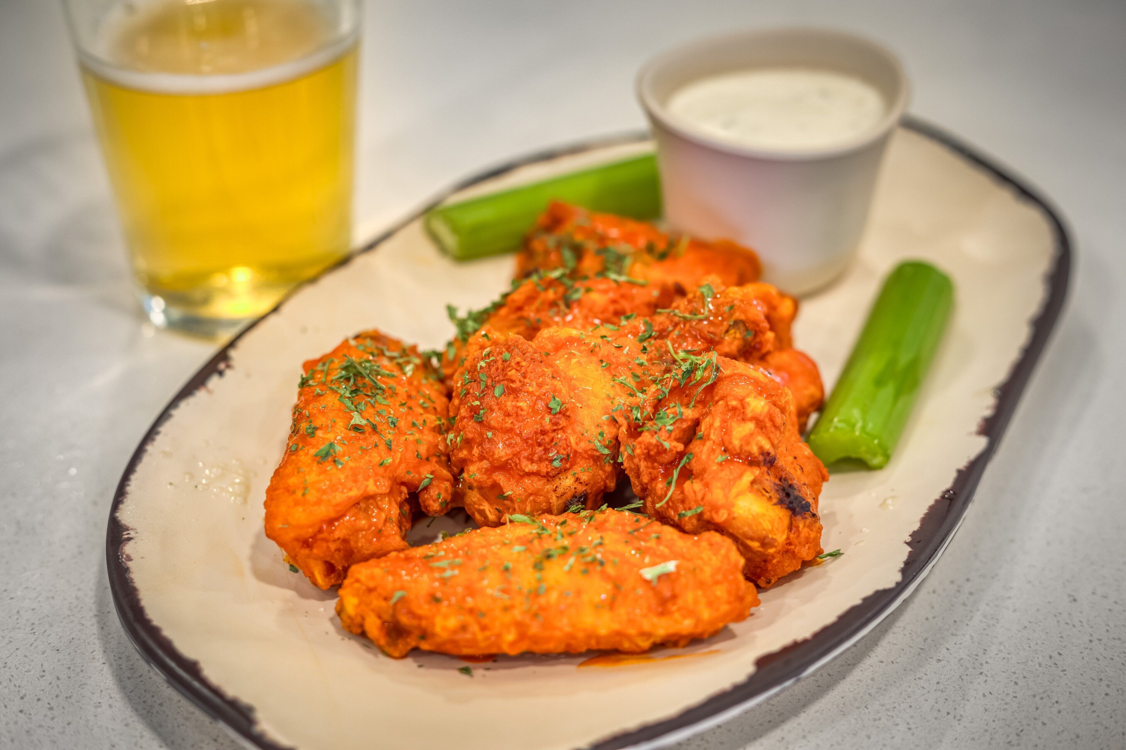 A plate of chicken wings with a side of celery and a cup of sauce.