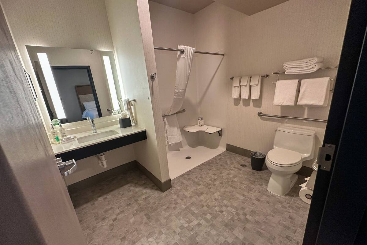 Een moderne badkamer met een wastafel, spiegel, douche, toilet en handdoekrek.