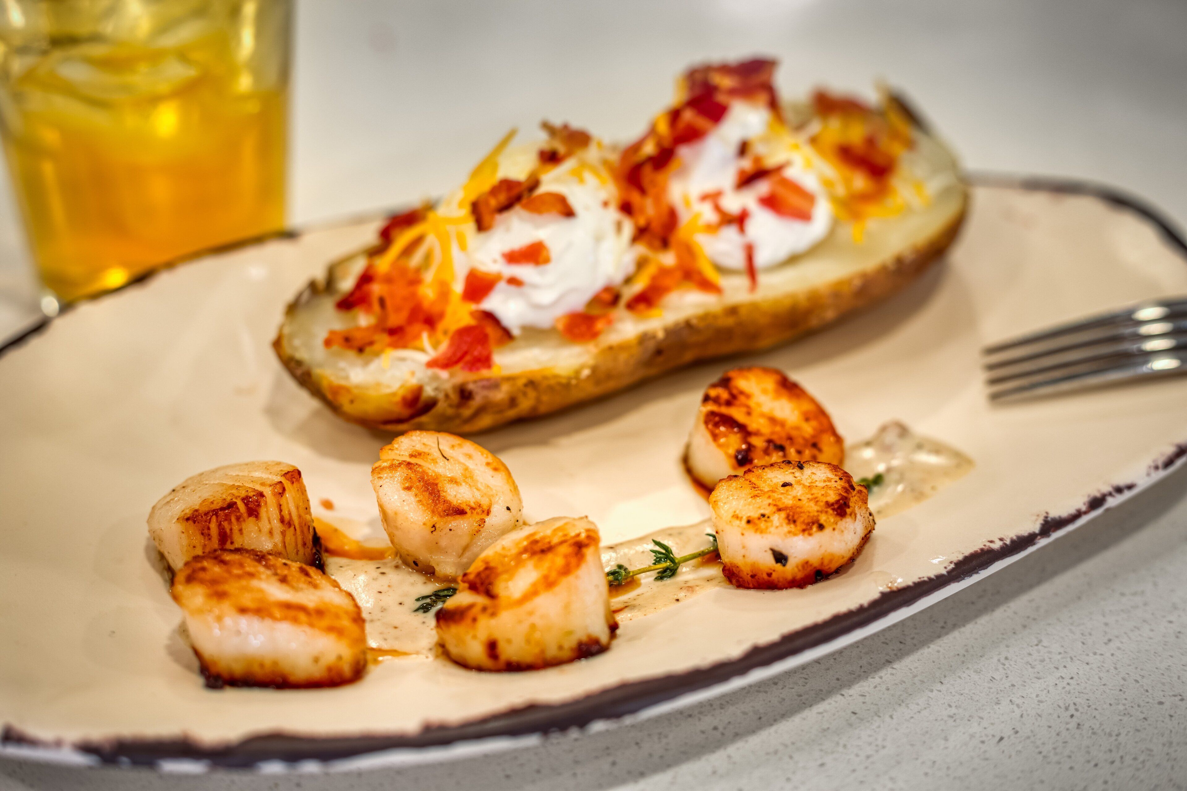 A plate with seared scallops and a breaded item topped with cheese and bacon.