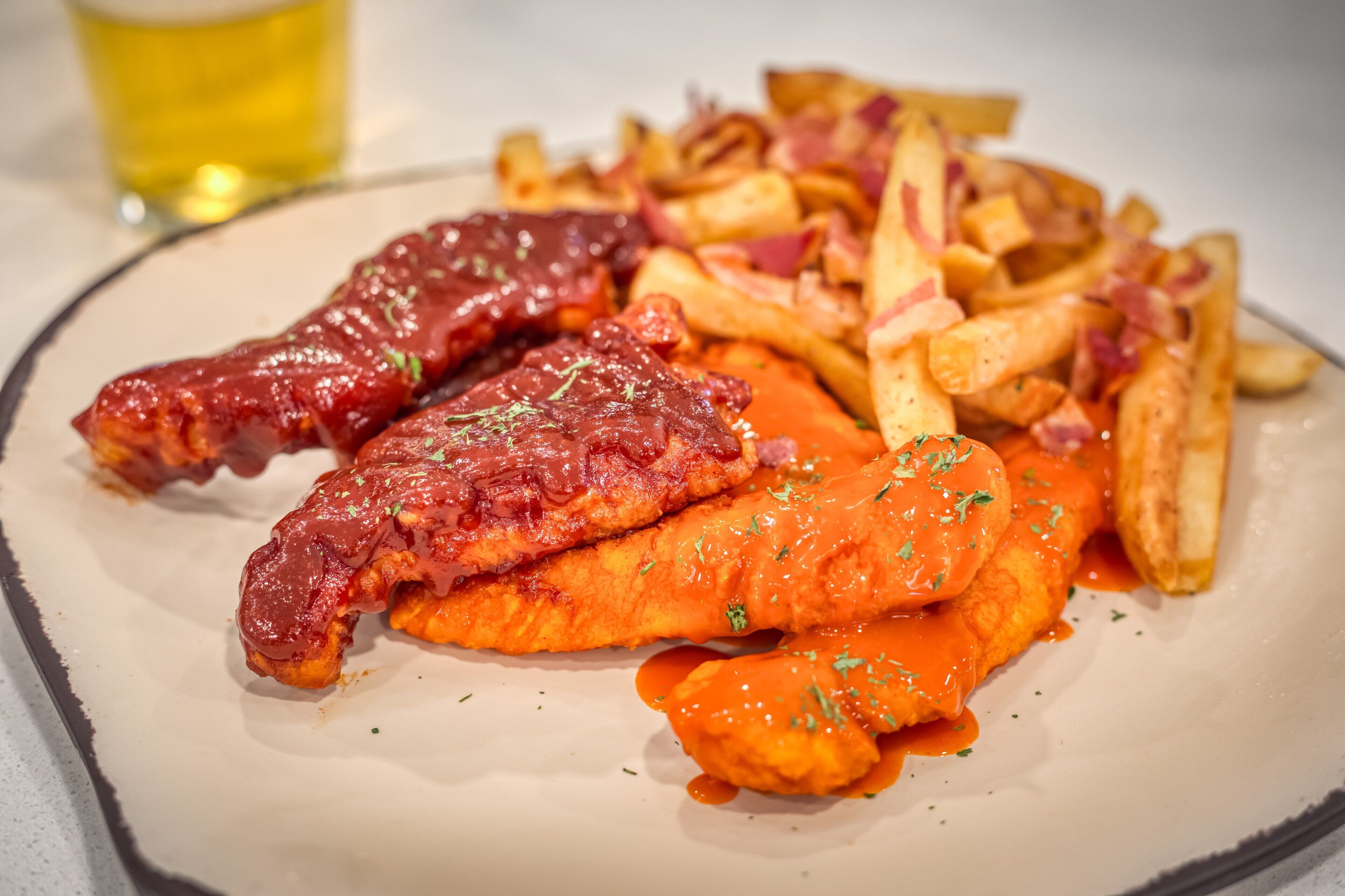 Ein Teller Essen mit zwei Fleischstücken, Pommes und einem Getränk.