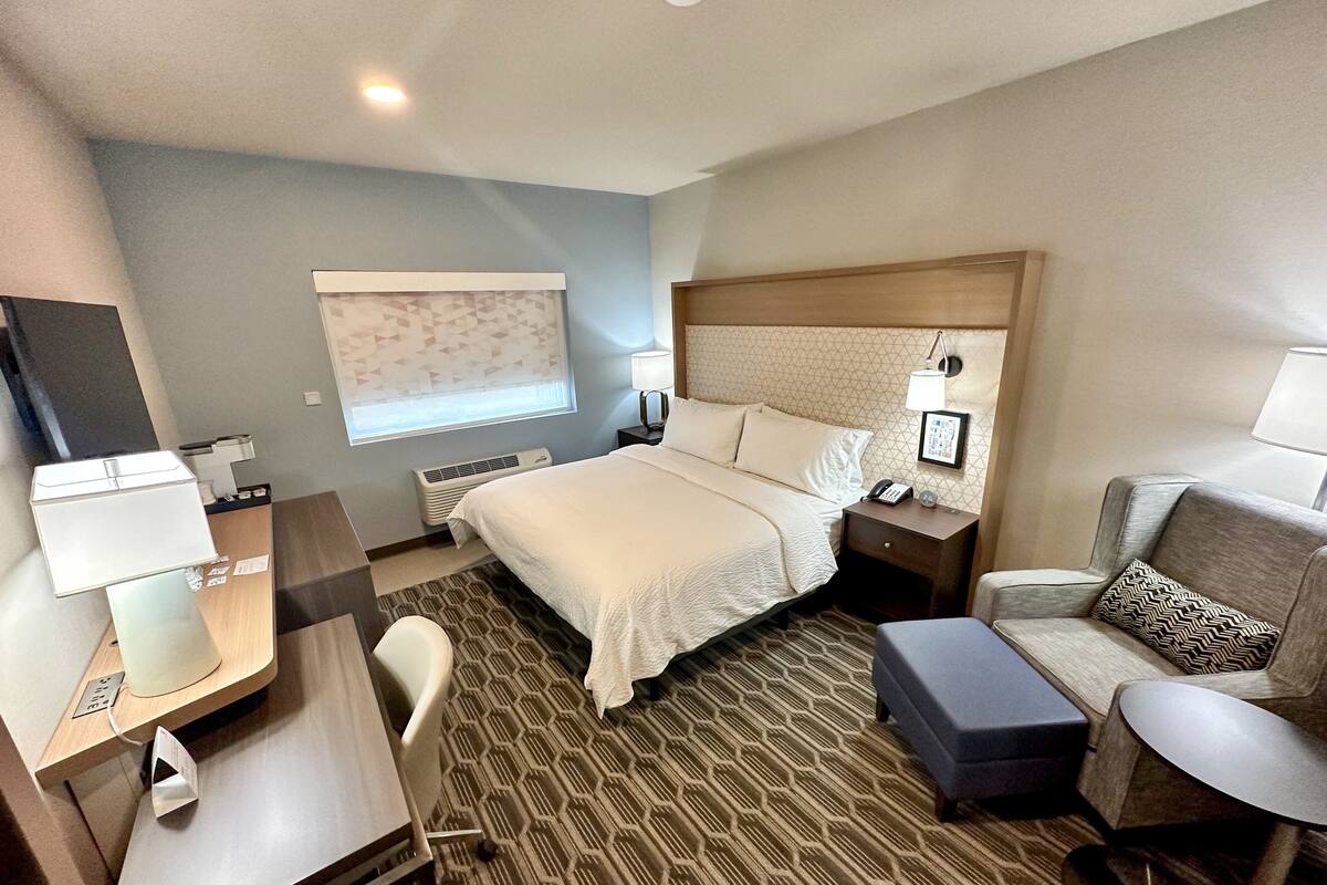 Een hotelkamer met een groot bed, een bureau met lamp, een stoel, een bank en een nachtkastje met telefoon en lamp.