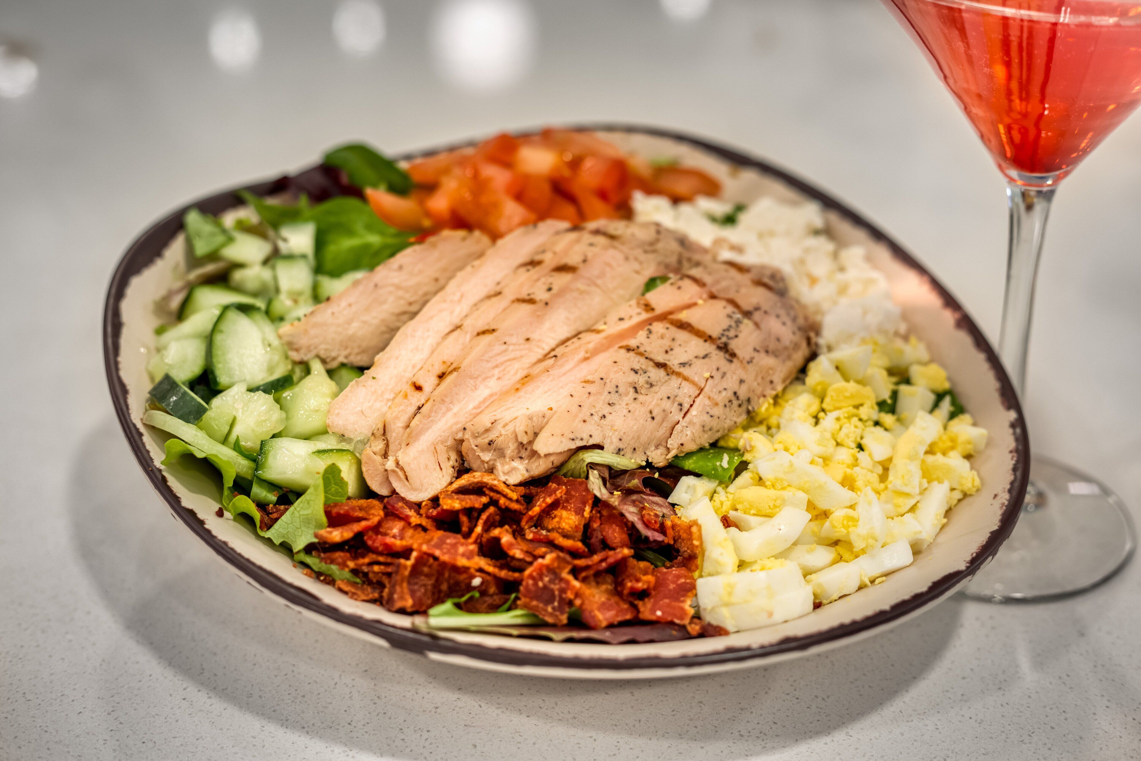 A plate of food with sliced chicken, vegetables, and eggs, accompanied by a glass of red drink.