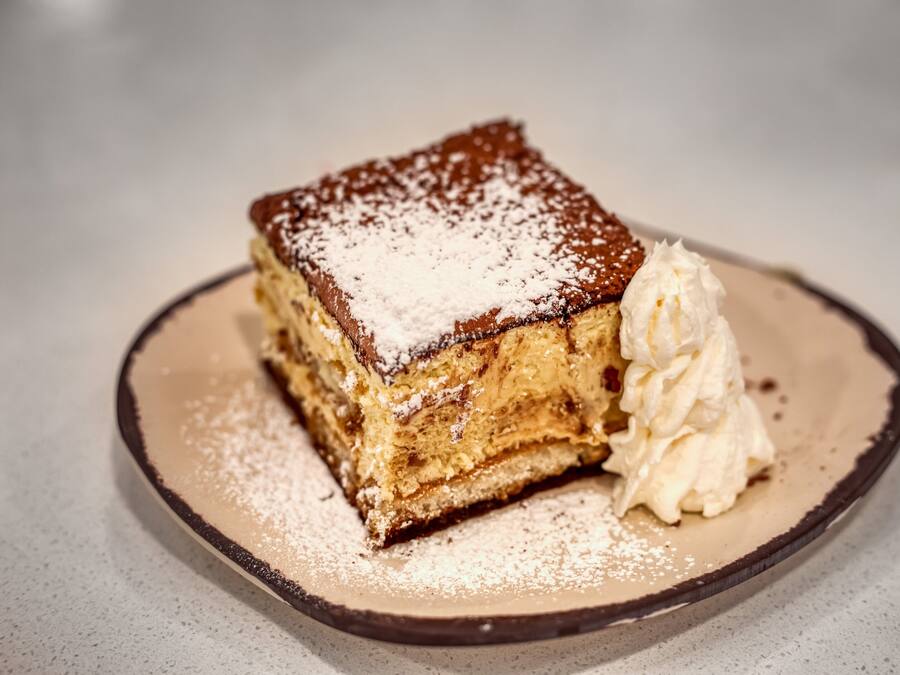 Una porción de postre en capas sobre un plato, con azúcar glas y una cucharada de crema batida.