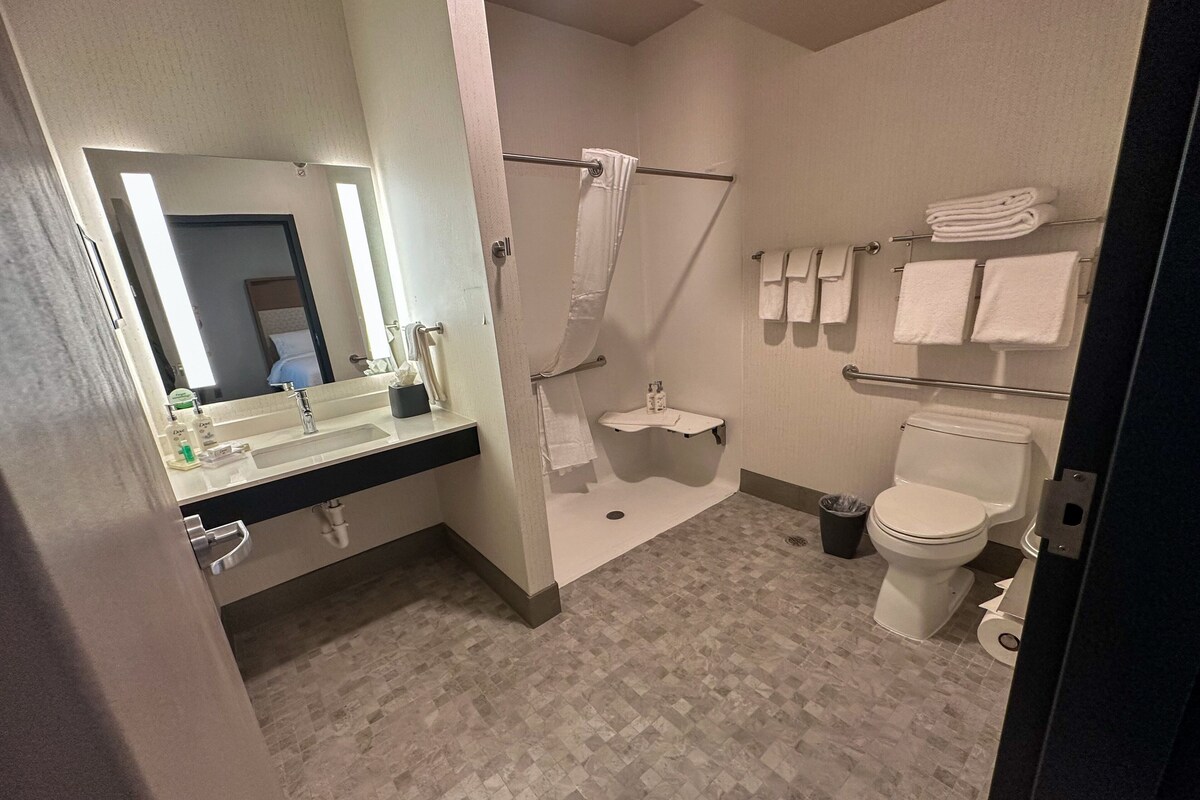 A modern bathroom with a sink, mirror, shower, toilet, and towel rack.