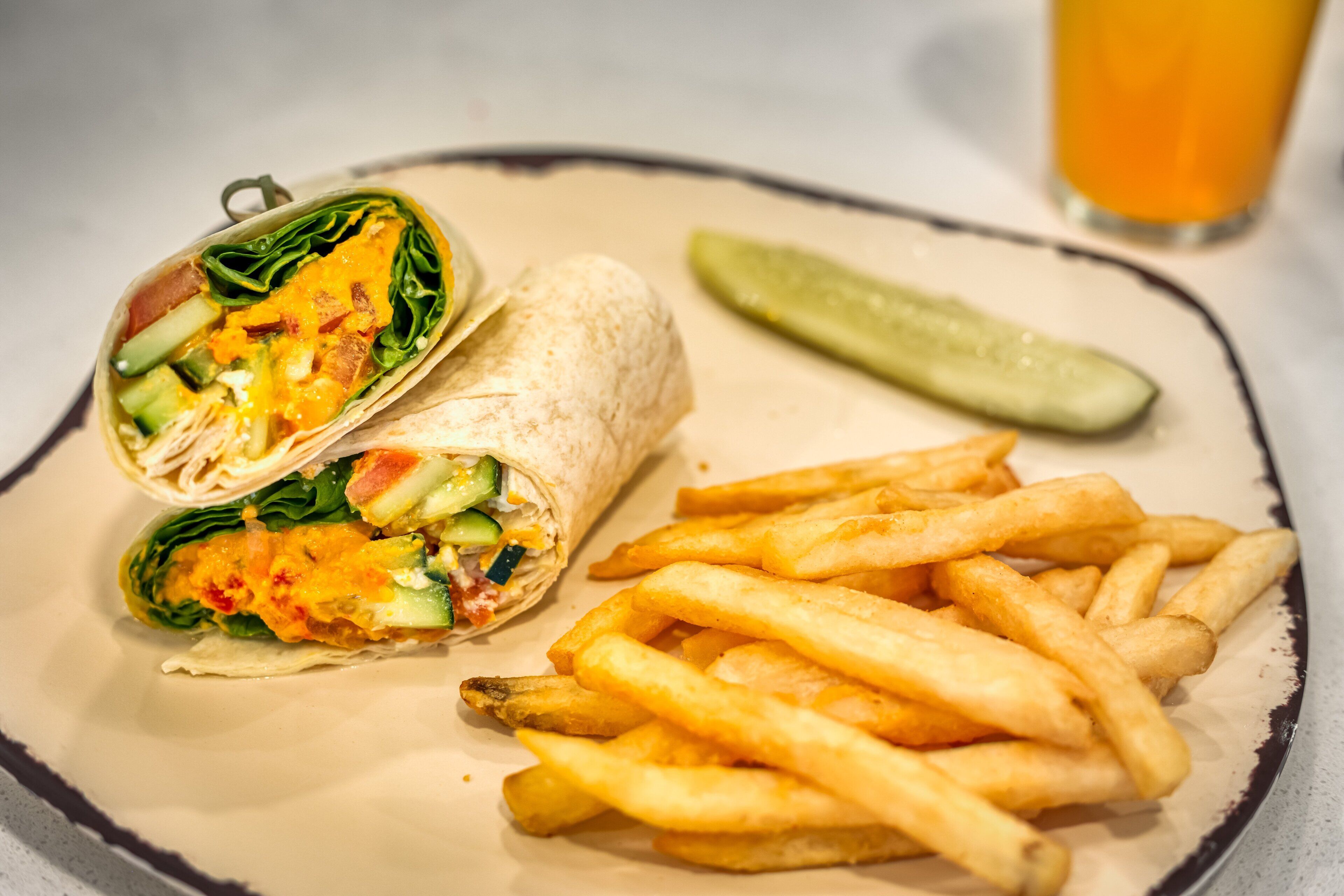 A burrito with fries and a pickle on a plate.