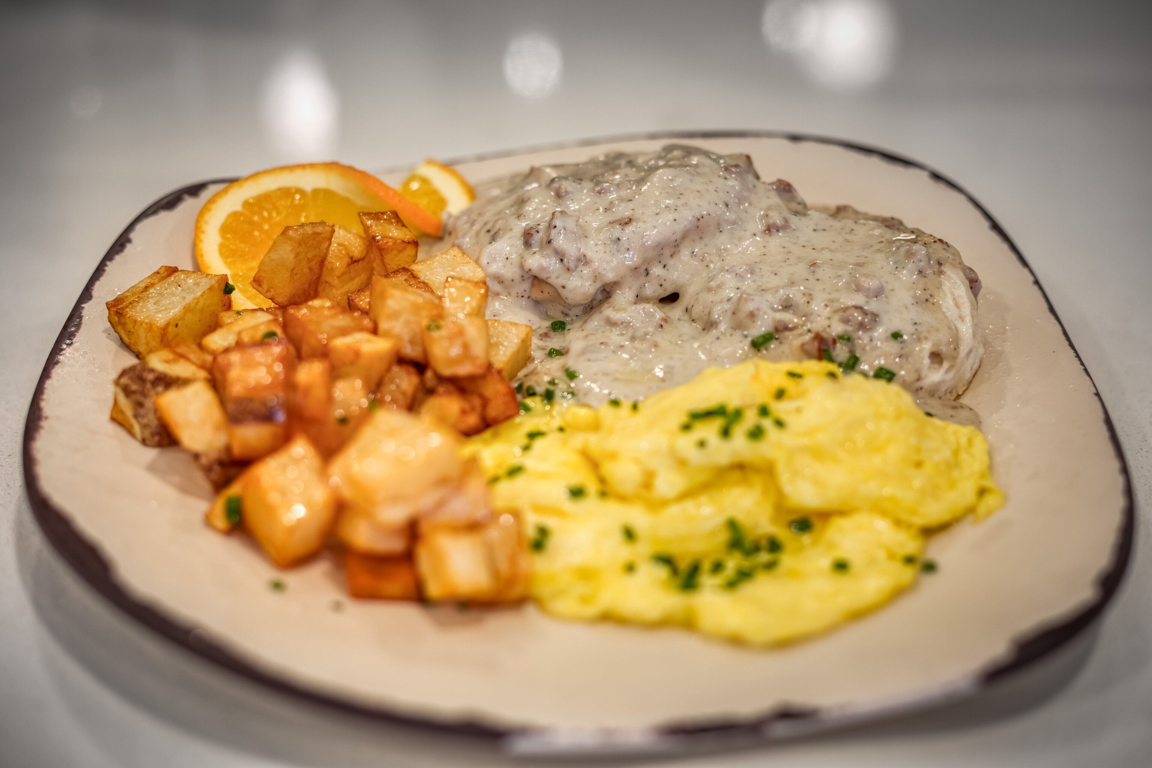 A plate of food with scrambled eggs, a meat dish with gravy, and roasted potatoes.