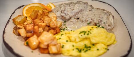 A plate of food with scrambled eggs, a meat dish with gravy, and roasted potatoes.