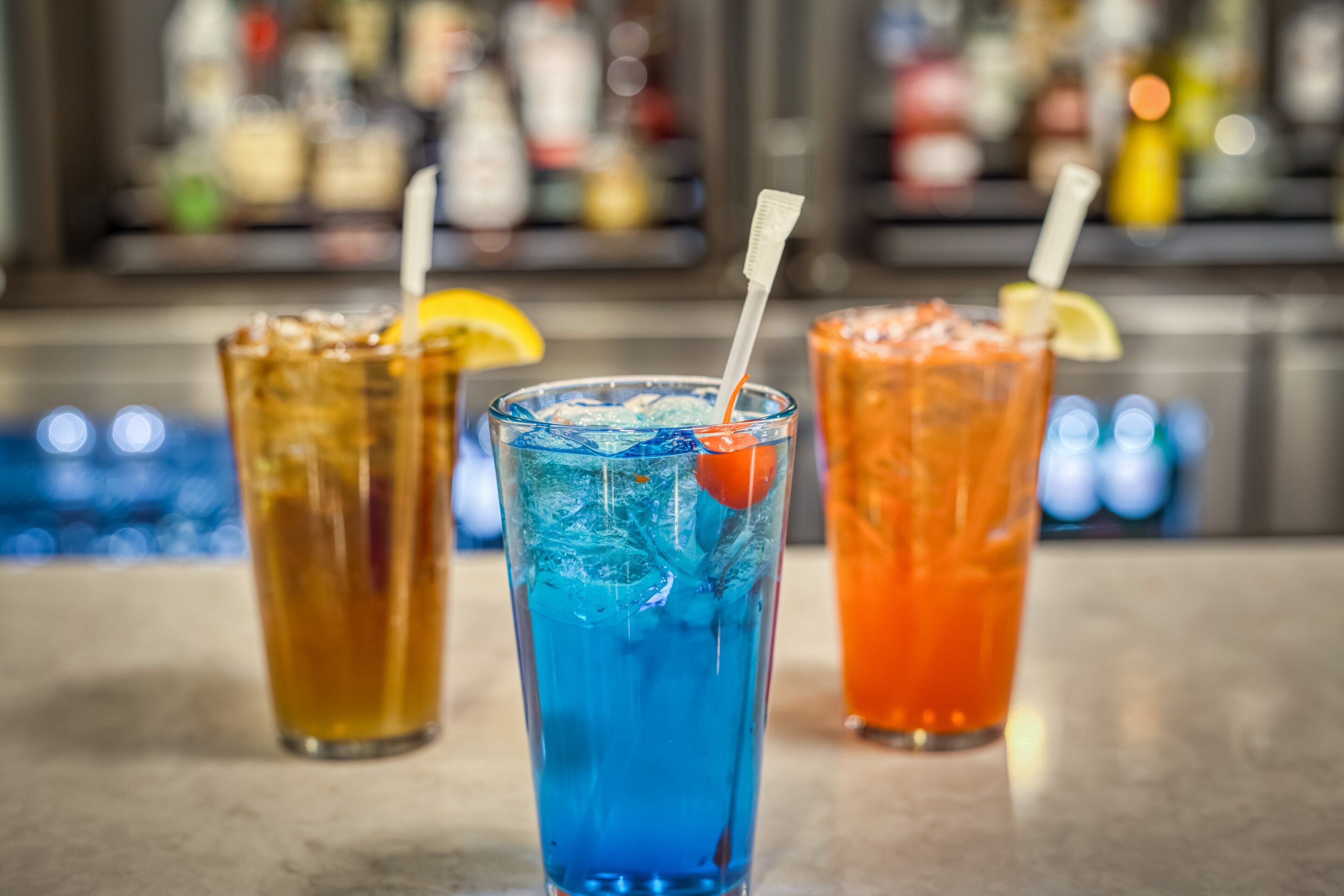 Tres vasos de bebidas con pajitas y rodajas de limón sobre una barra.