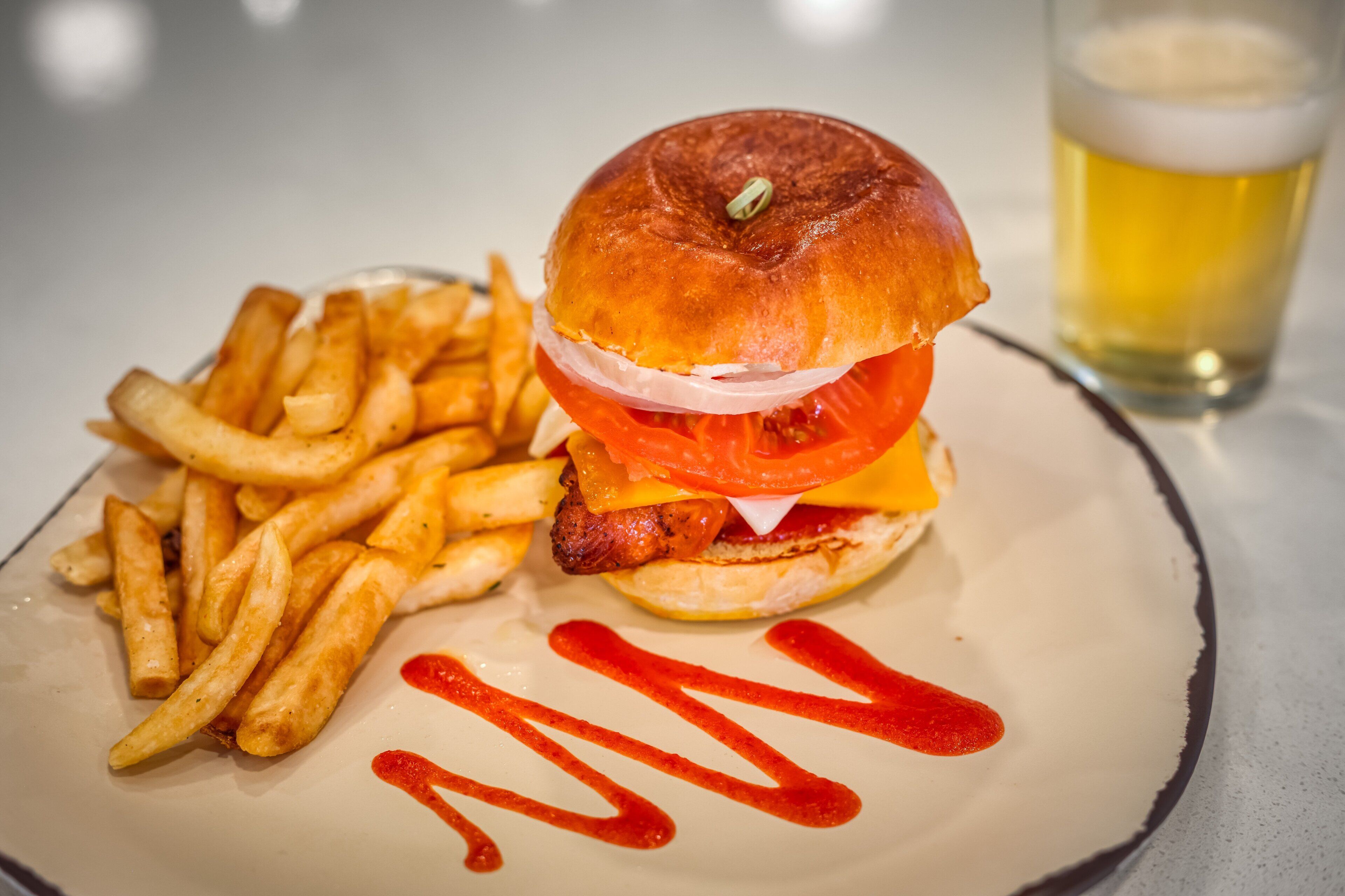 A burger with fries and a glass of beer on a plate.