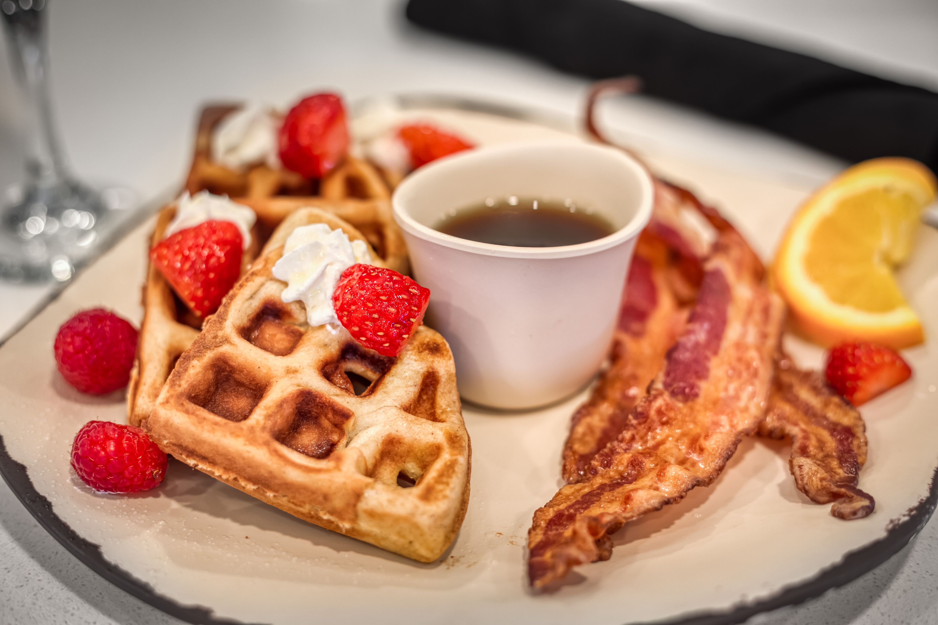 Une assiette avec des gaufres, du bacon, des fraises et une tasse de café.