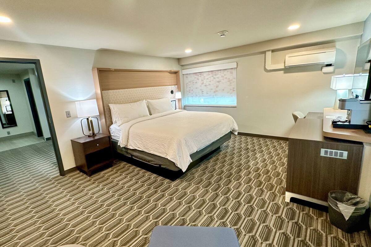 Een hotelkamer met een bed, een bureau, een prullenbak en een raam met jaloezieën.