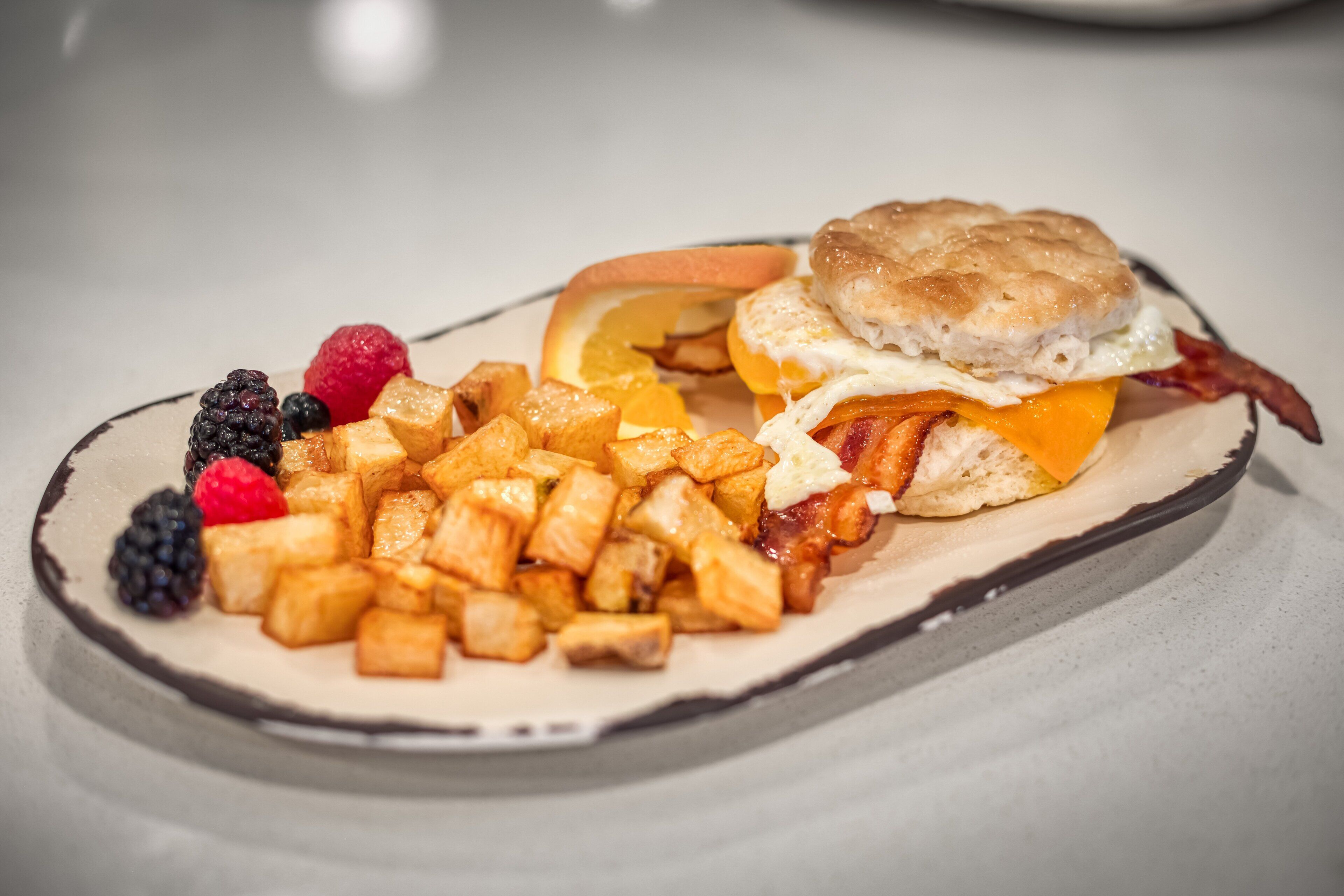 Un plato de desayuno con sándwich de galleta, huevos fritos, tocino, patatas ralladas y frutos rojos.